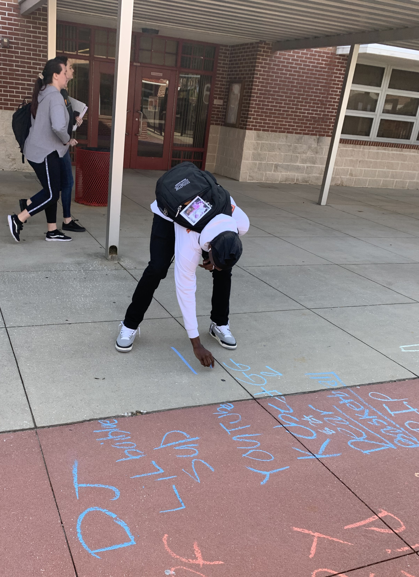 A Seabreeze High School student writes on the sidewalk in chalk for 
