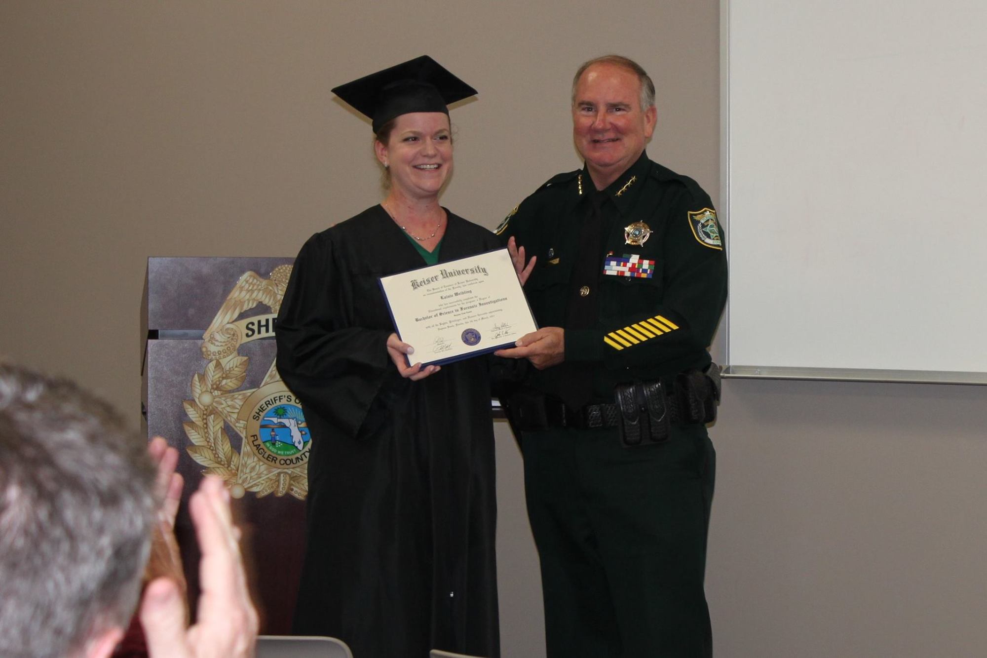 FCSO CSI Lainie Weibling smiles with her Keiser University degree with Sheriff Rick Staly. Photo courtesy of FCSO Facebook