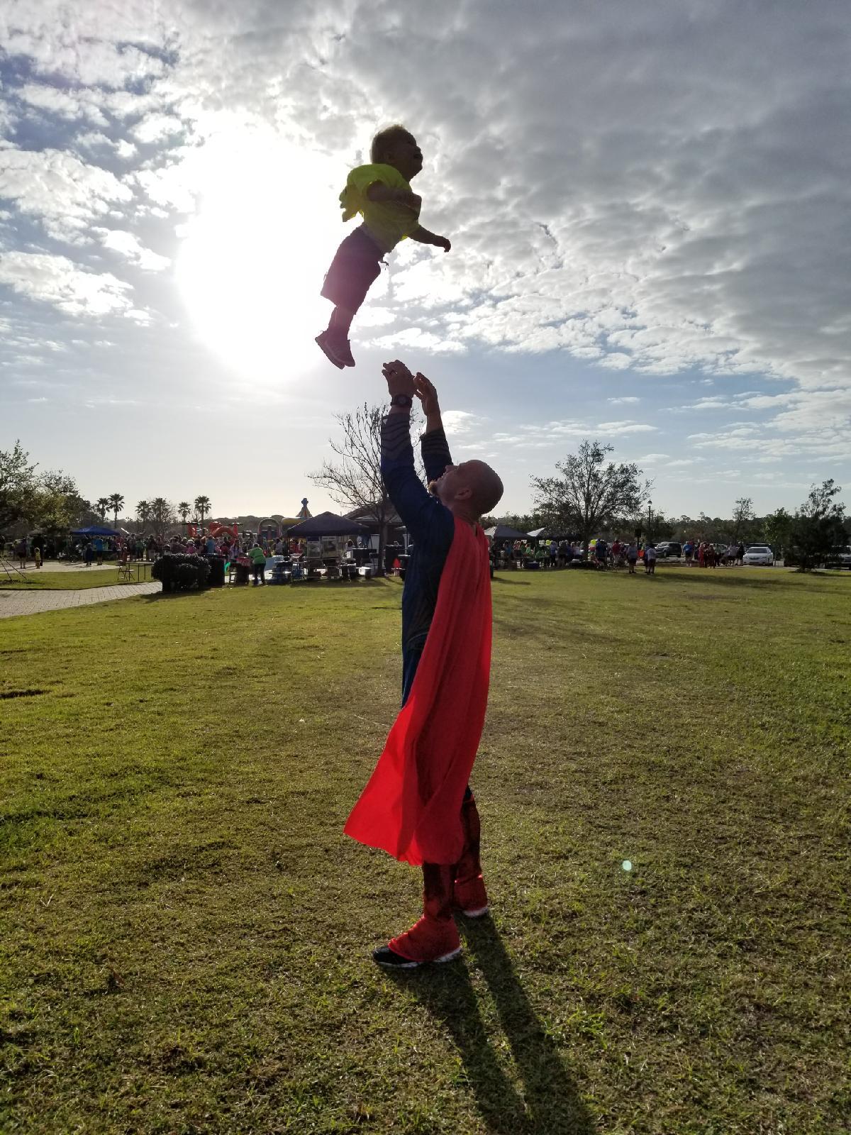 Elijah Hopkins, as Superman, tosses his son Gabriel into the air playfully at the Superhero 5K. Photo courtesy of Julie Davis