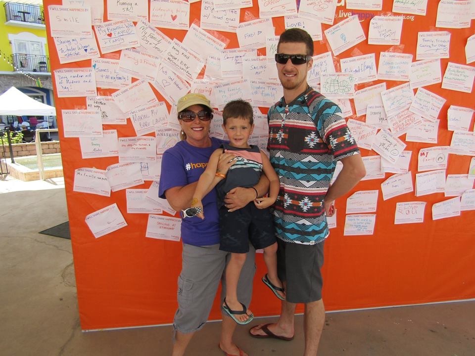 Sue Goldberg with Luca Morreale, 3, and his father Joseph Morreale pose in front of the Happiness Wall. Photo courtesy of Sue Goldberg