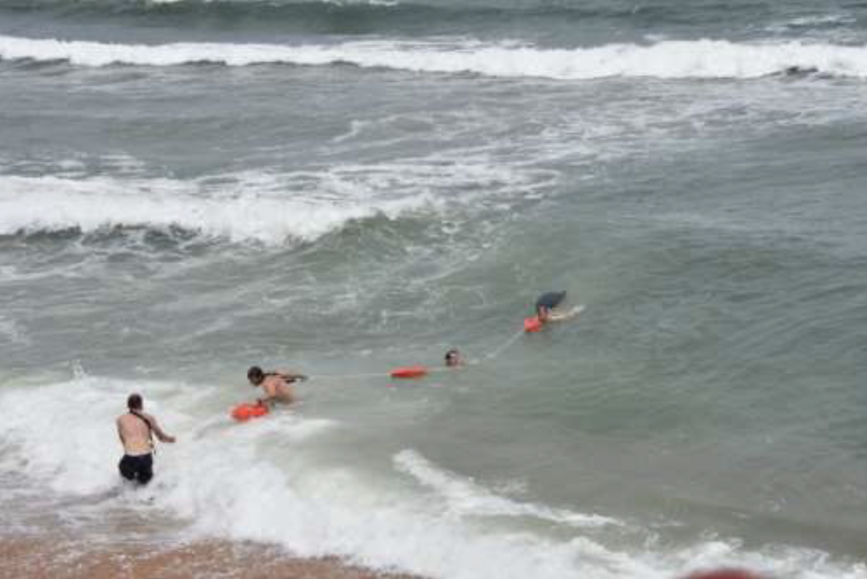 Lifeguards form a human chain to rescue a woman caught in a rip current, visible here running perpendicular to the breakers. Image courtesy of the city of Flagler Beach