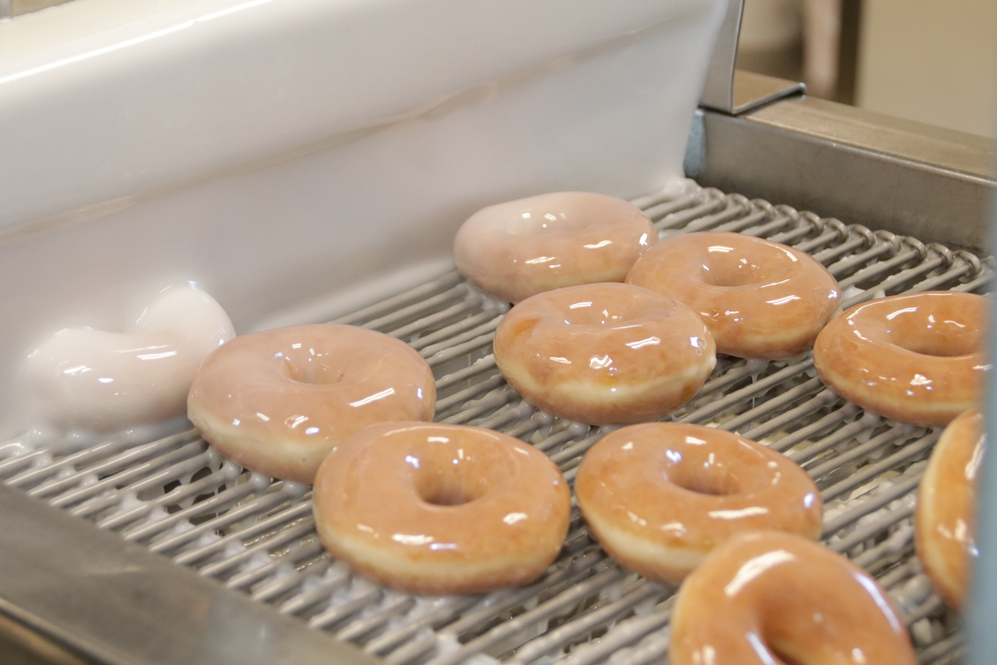 Freshly cooked doughnuts emerge from the wall of glaze. JimJett.com photo
