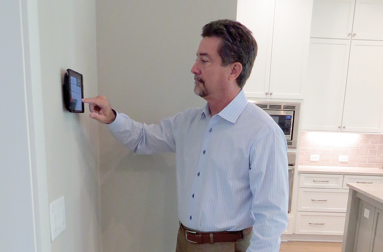 Glenn Layton demonstrates smart home controls from the wall-mounted tablet in his Twenty Mile Village home. The tablet can be removed and taken anywhere without losing connectivity to home automation devices.