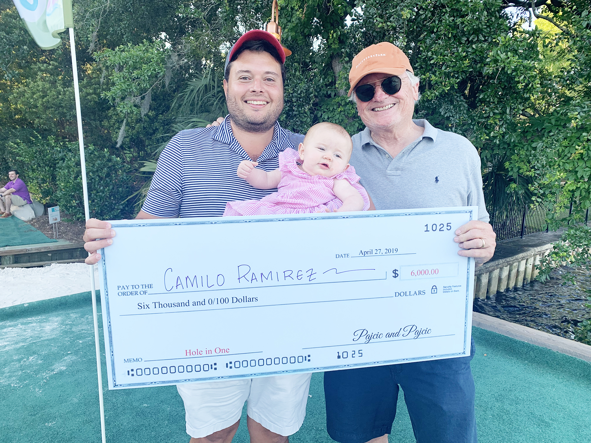 Special to the Daily Record Camilo Ramirez, left, won a $6,000 prize by sinking a hole-in-one at the yard golf event presented by the Pajcic & Pajcic law firm. He’s shown with 8-month-old daughter, Reid, and attorney Steve Pajcic.