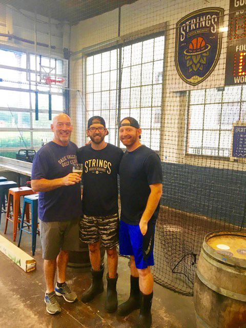 Scott, Colby and Trevor Adeeb in front of the basketball hoop inside Strings Sports Brewery.