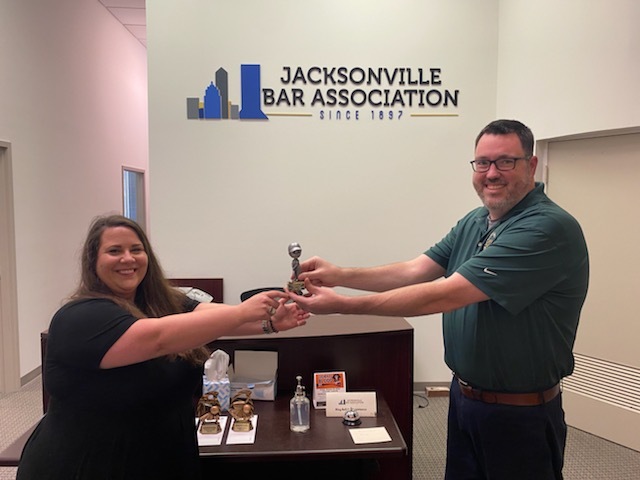 Attorney Kathryn Stanfill accepts, properly socially distanced, the first-place trophy for the Jacksonville Bar Association miniature golf tournament at the Oct. 16 barbecue from JBA Executive Dorector Craig Shoup.