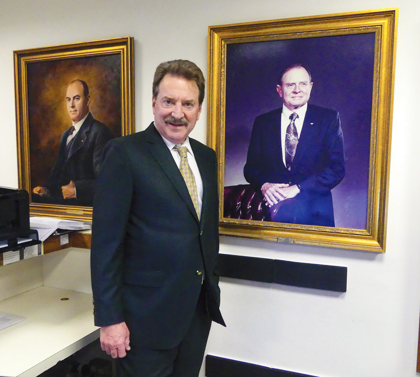 Cecil W. Powell & Company President Fitzhugh Powell Jr. with portraits of his grandfather, Cecil Powell, and his father, Fitzhugh Powell Sr., that are displayed in the insurance agency’s offices.
