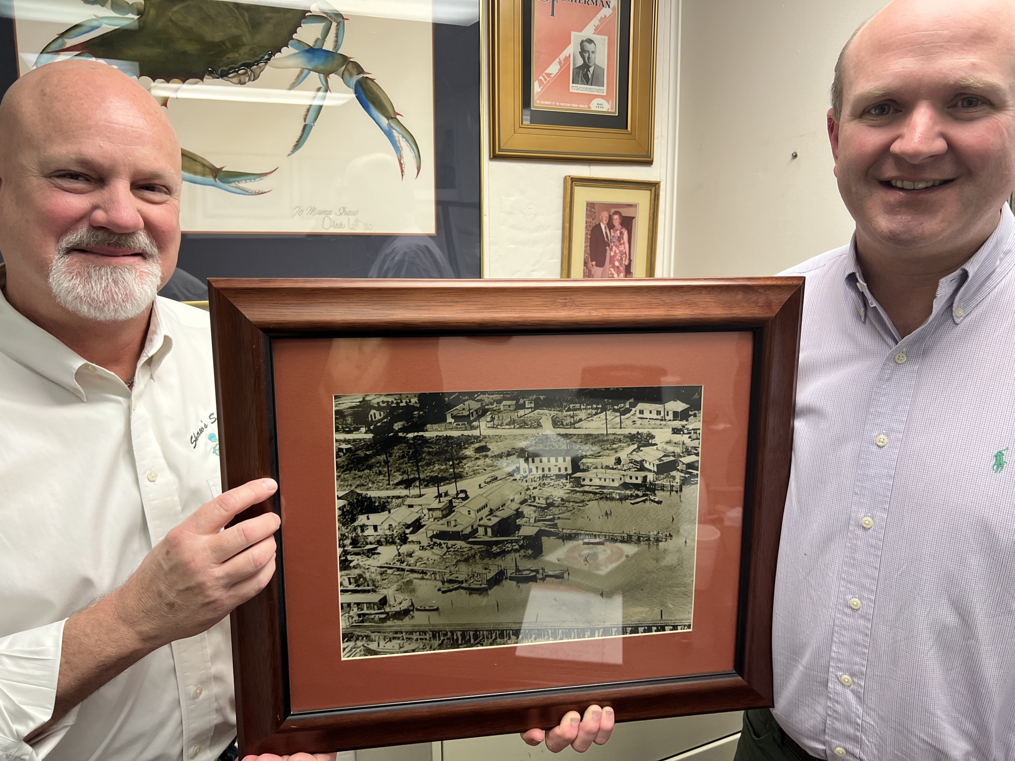 Howard “Bubba” Shaw Jr.  and John Shaw III hold a picture of their company’s original plant along the Trout River.