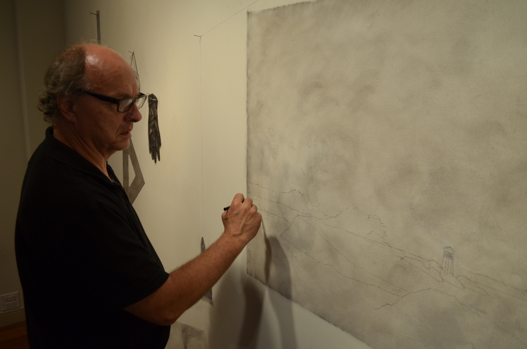 Patrick Lindhardt using charcoal and creating a series of landscapes right on top of the gallery wall.