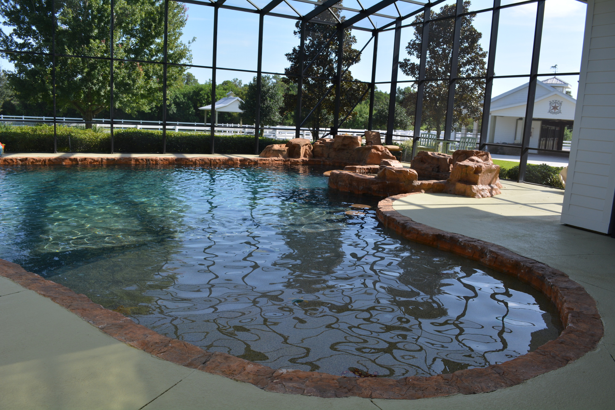 The customized lighted pool and spa has a two-tone pebble ted surface, swim-out and sitting areas, two in-water tide stools that face a television, a waterfall and a complete outdoor kitchen with a gas commercial grill and stove and a refrigerator.
