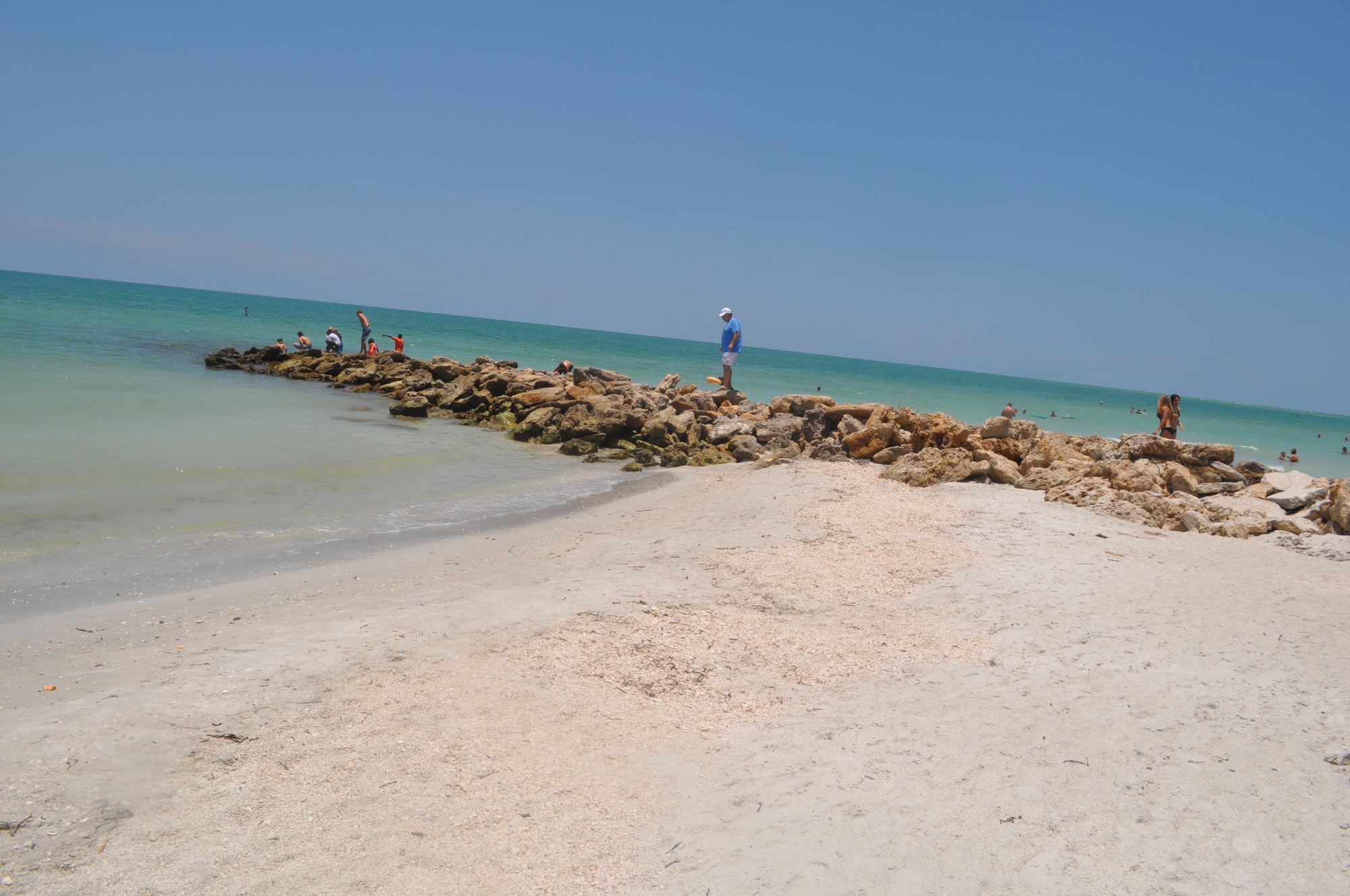 Beachgoers walk along an exposed rock jetty on Lido Key that was submerged in sand last year.