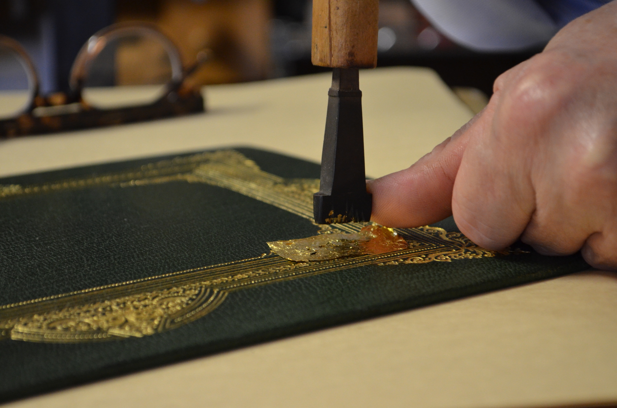Tapley presses a piece of gold leaf into a dark green leather cover.