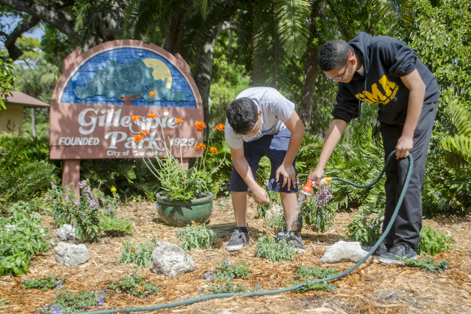 Diego Leon and Quinn Selby Gomez water flowers in front of the Gillespie Park sign. 