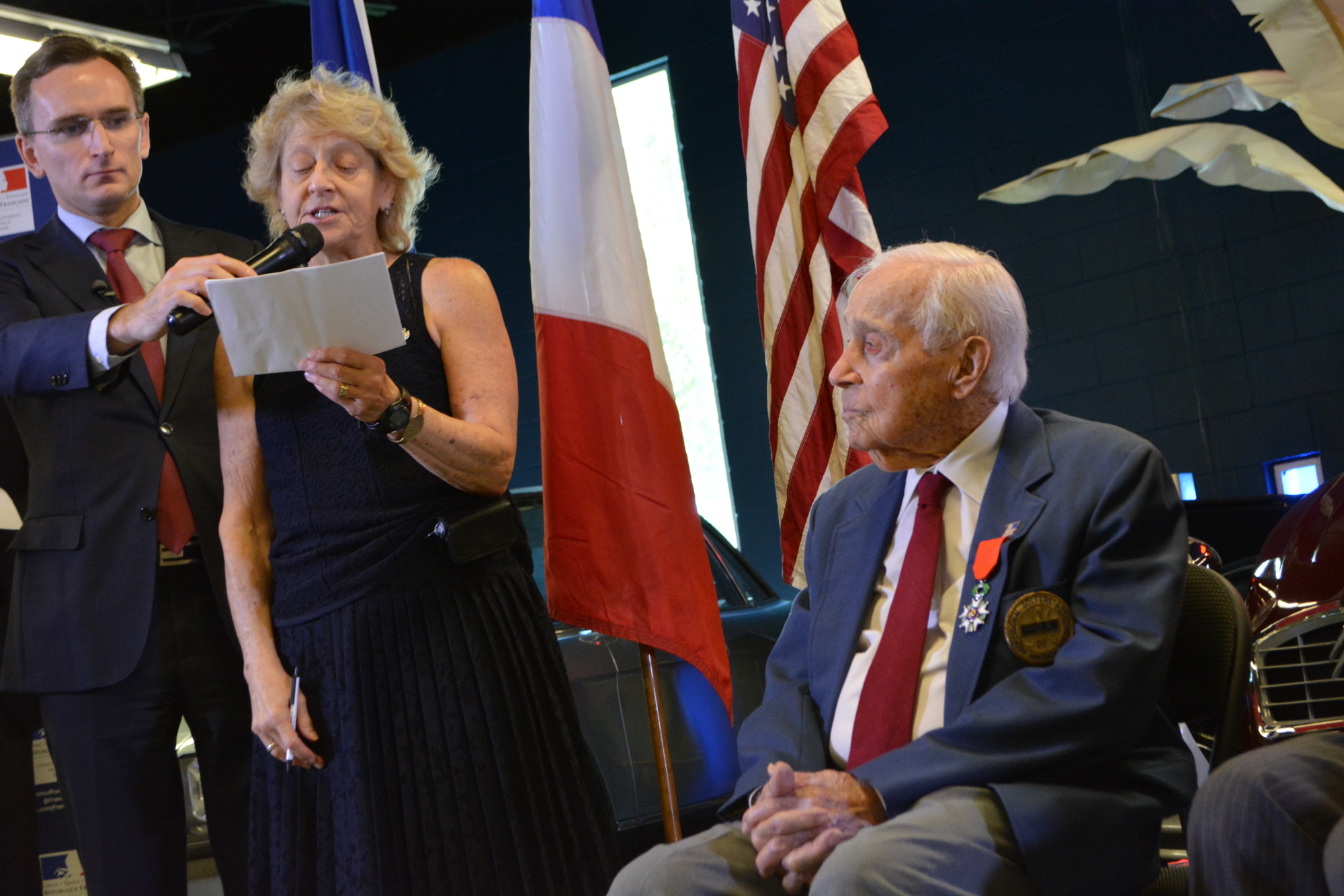 Teresa Andreone, Gus Andreone's niece, reads comments on his behalf during the ceremoney. Andreone, seated, thanked France for the honor and the French people's hospitality during the war.