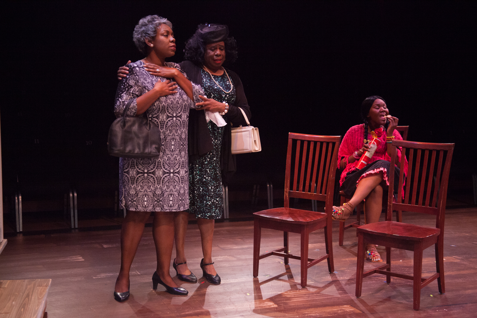 The wife, Raynelle (Dee Selmore) and sister, Marguerite (Nate Jacobs) of the deceased comfort one another, while Delightful (Kourtney McLaughlin) has a snack. Photo by Don Daly.