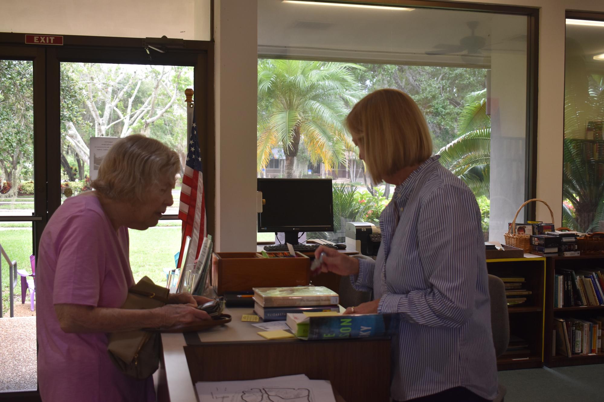 Barbara Moscow, who comes to the library every week, checks out a book from Linda Lutz.