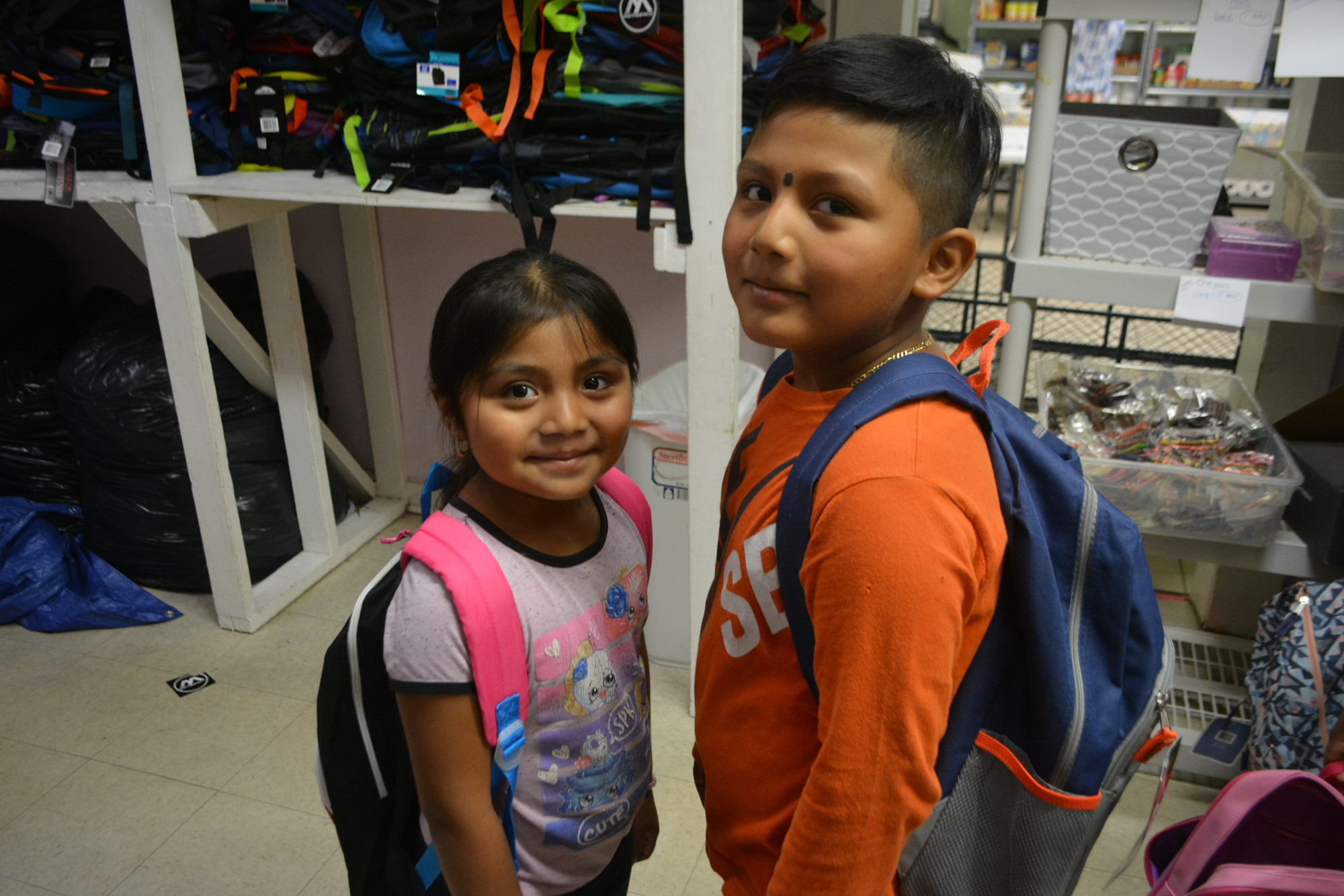 Six-year-old Sheila Perez and her brother, 8-year-old Yovani Perez, show off the backpacks they picked up at the Stillpoint House of Prayer on Monday.