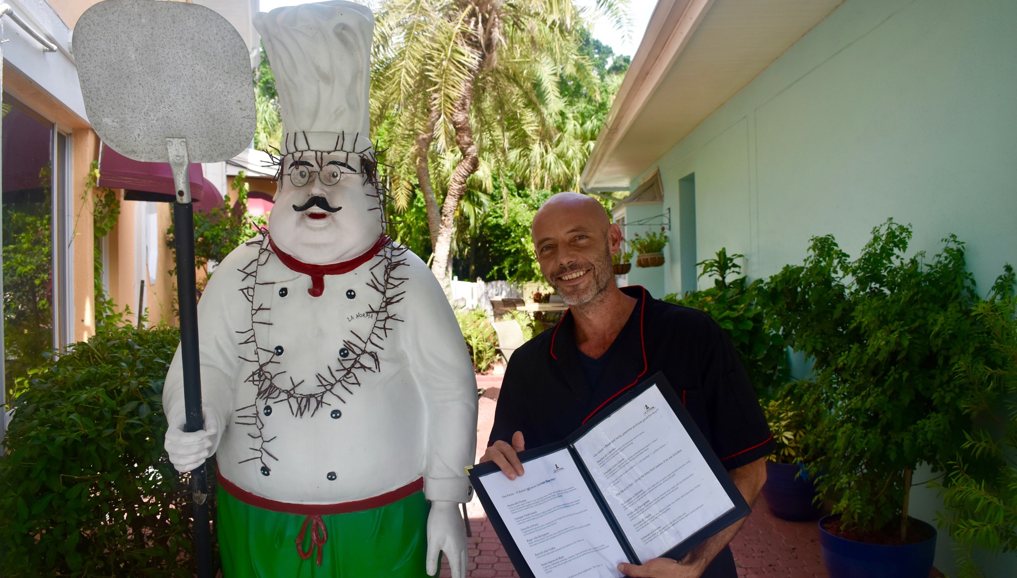 Gianfranco Santagati poses in front of La Norma with the restaurant menu and its mascot.