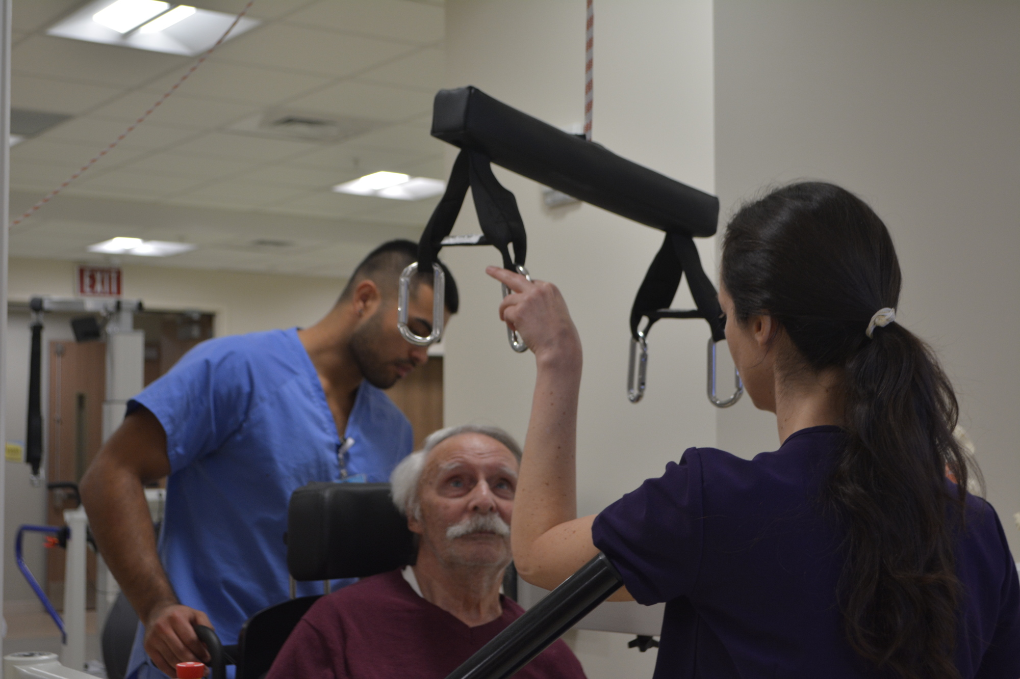 Stroke patient Ronald Serres (seated) watches as physical therapist Dr. Julia Figueroa (right) and rehab tech Daniel Gonzalez strap him into the Hocoma Lokomat. The Lokomat controls the amount of weight Serres feels on both sides.
