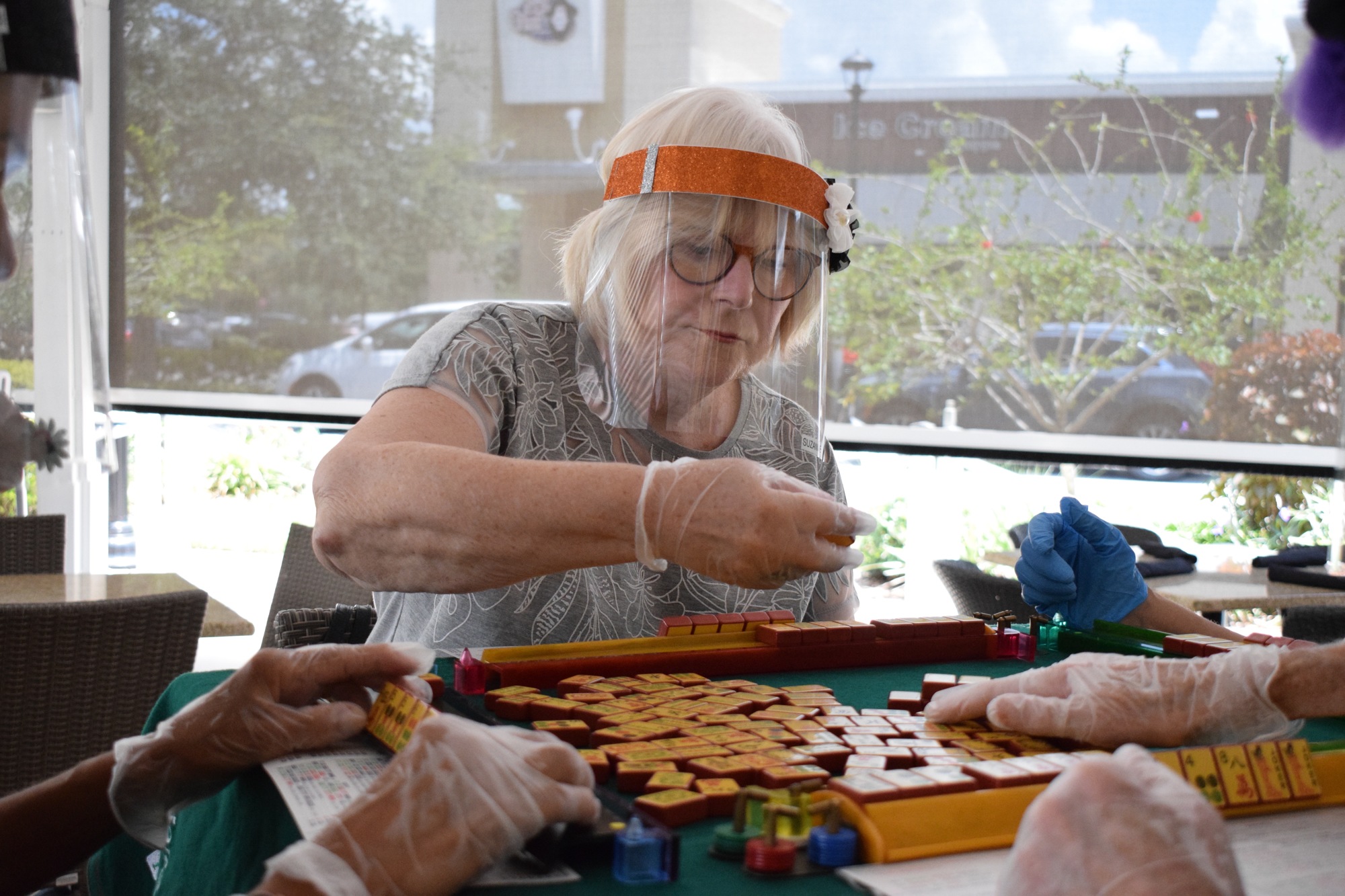 Riverwalk's Suzanne Weitz places a tile down while playing mahjong. The group plays while wearing a mask or face shield and gloves as a precaution.