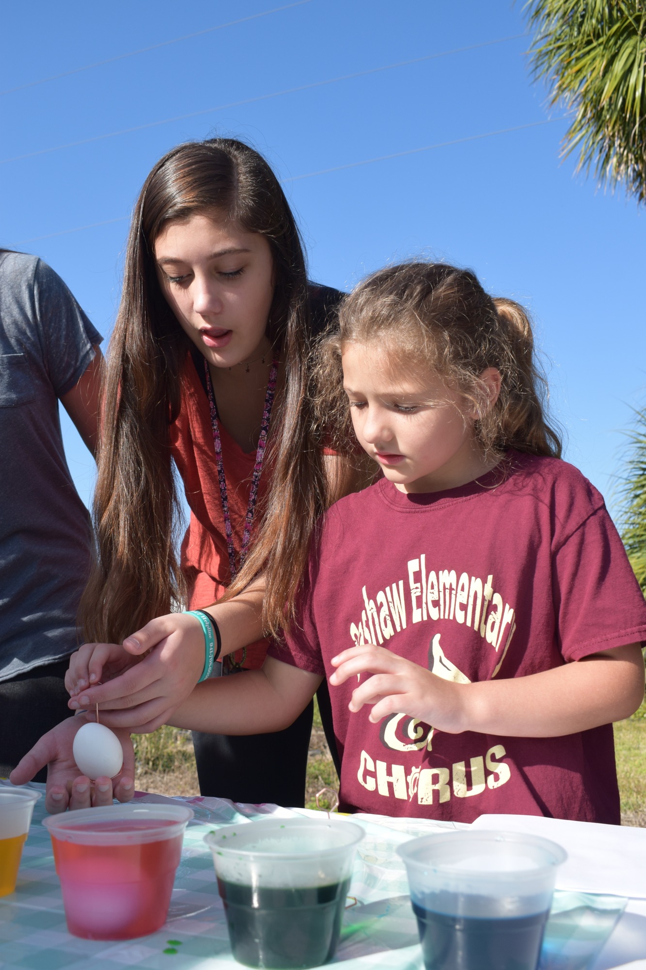 Kenley Greenleaf, a sophomore at Braden River High School, helps Cayleigh Greer, a fourth grader at William H. Bashaw Elementary School, dye an egg during an event last year. File photo.