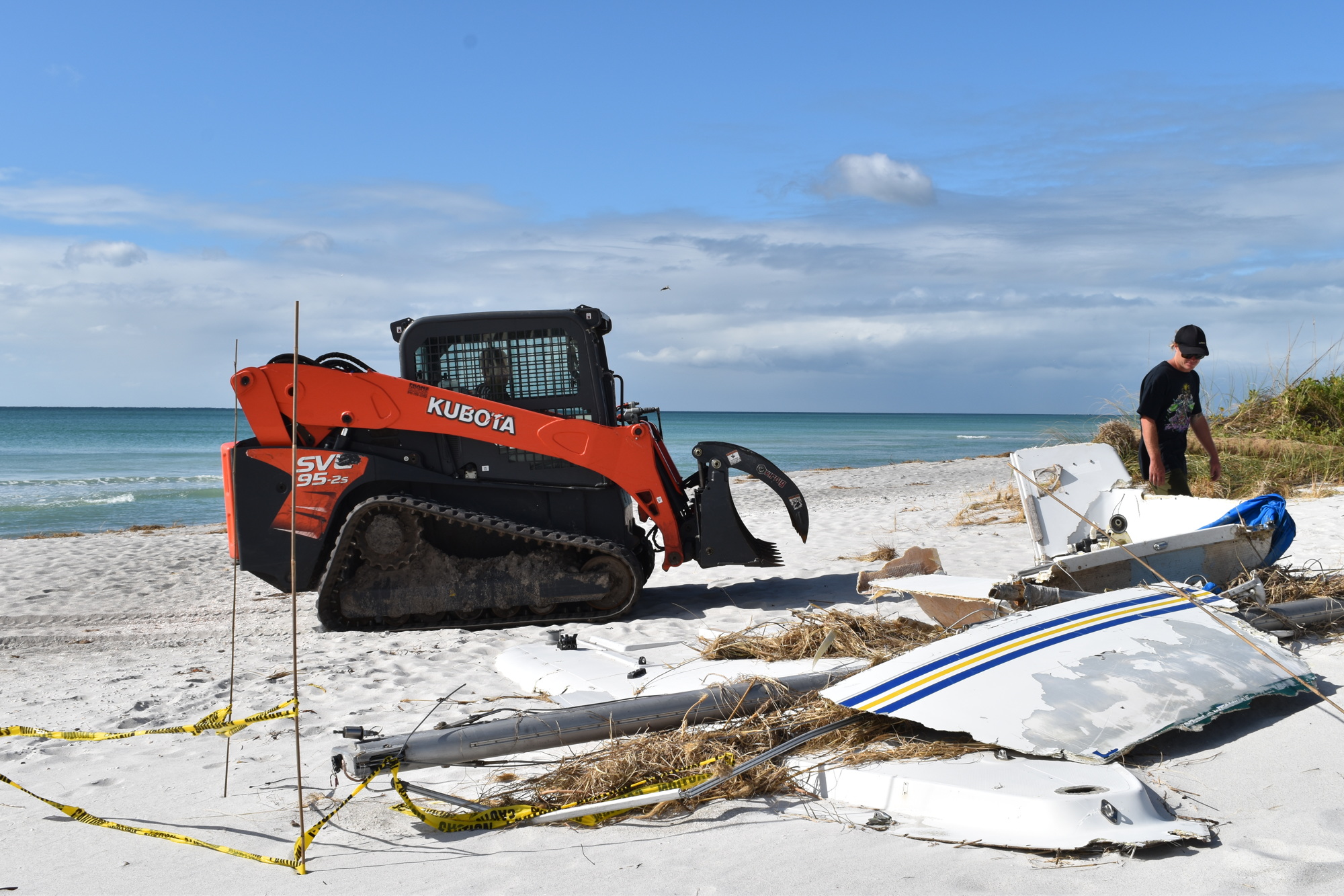 Sea Tow owner Duke Overstreet operates a Kubota skid steer to dismantle the sailboat debris that washed ashore. Sea Tow employee York Graham looks on.
