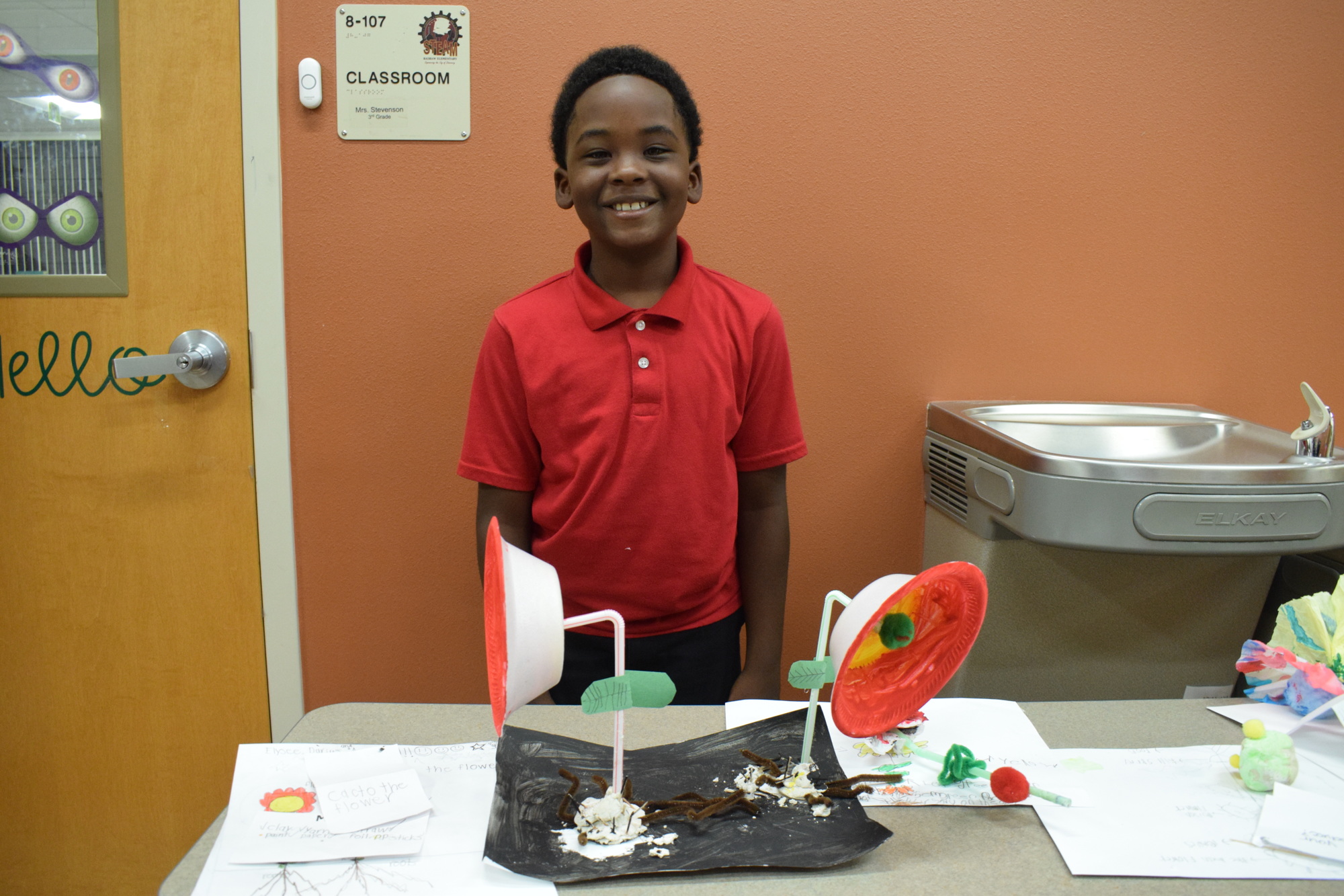 Elysee Thelusma, a third grader, shows off the plant he created using clay, straws, paper, foil, pipe cleaners and other items. He calls it 