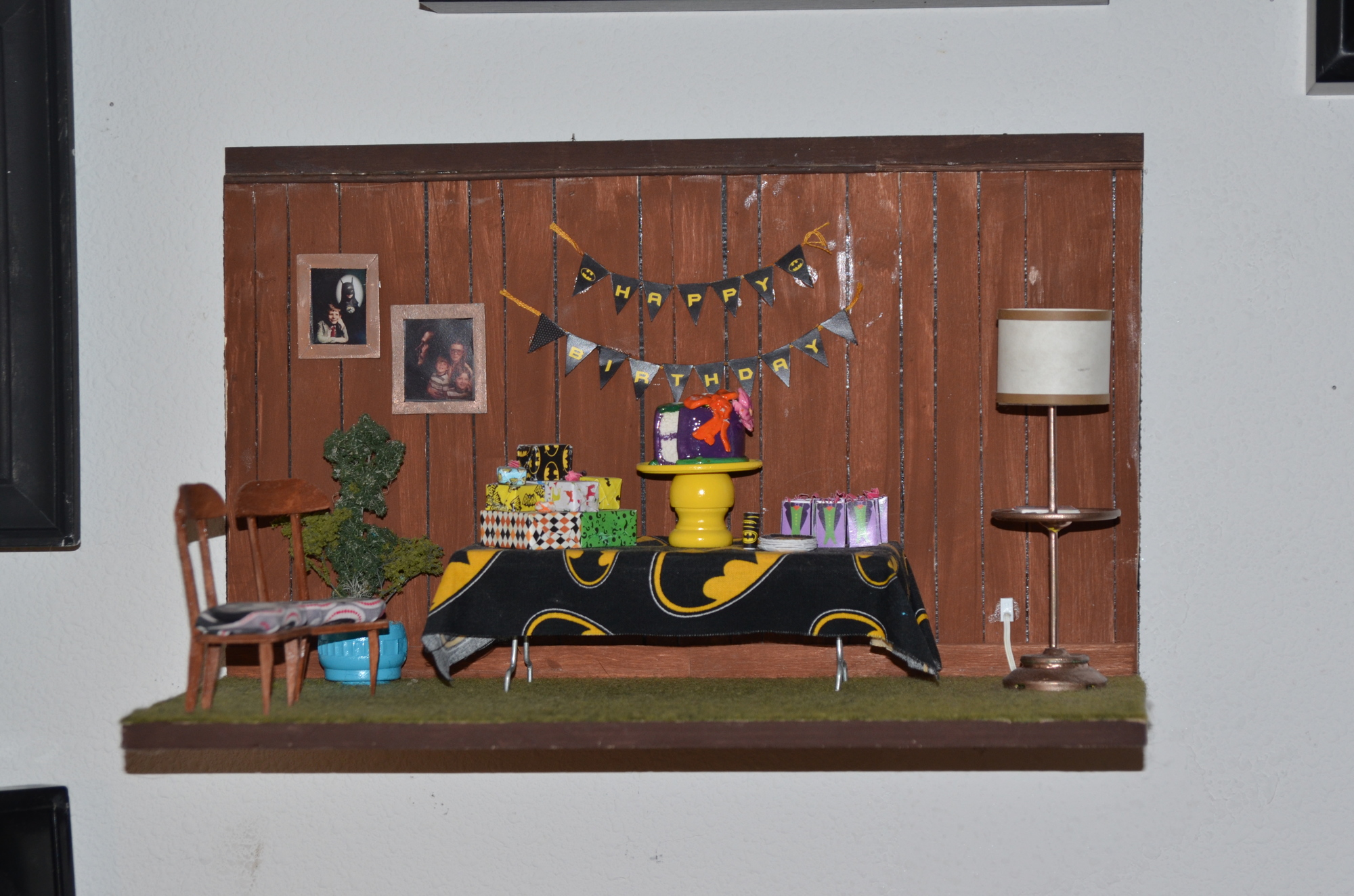 As the story in this miniature goes, a boy invited nine guests to his birthday party, and they all showed up with gifts. Details include the family portrait on the wood-paneling wall and Grandma’s glasses and cards on the side table.