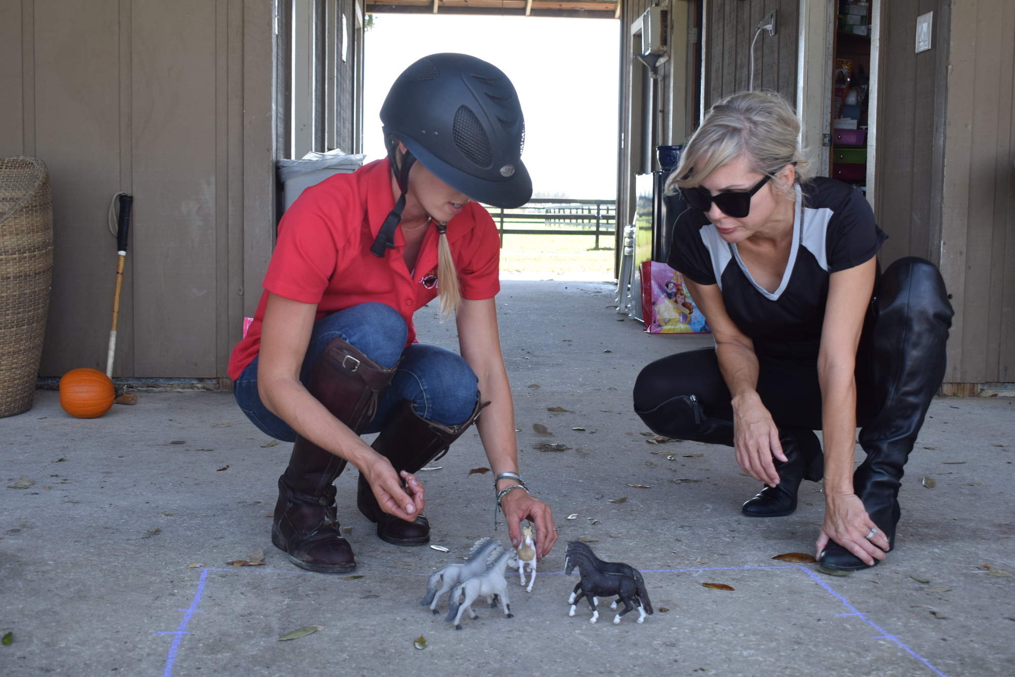 Ashlie Osburg and Karen Medford go over polo positioning with toy horses before Medford's first lesson.