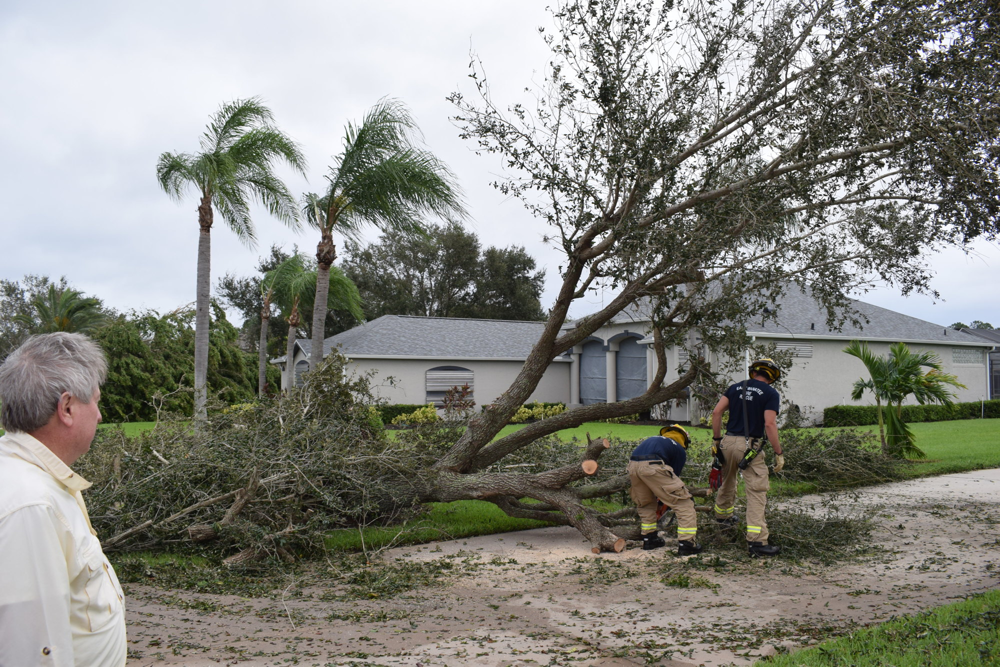 River Club's Fred Nelson watches as East Manatee Fire Rescue workers clear a tree from his driveway. He thanked Battalion Chief Charles Reid for responding so quickly.  (Photo by Jay Heater)
