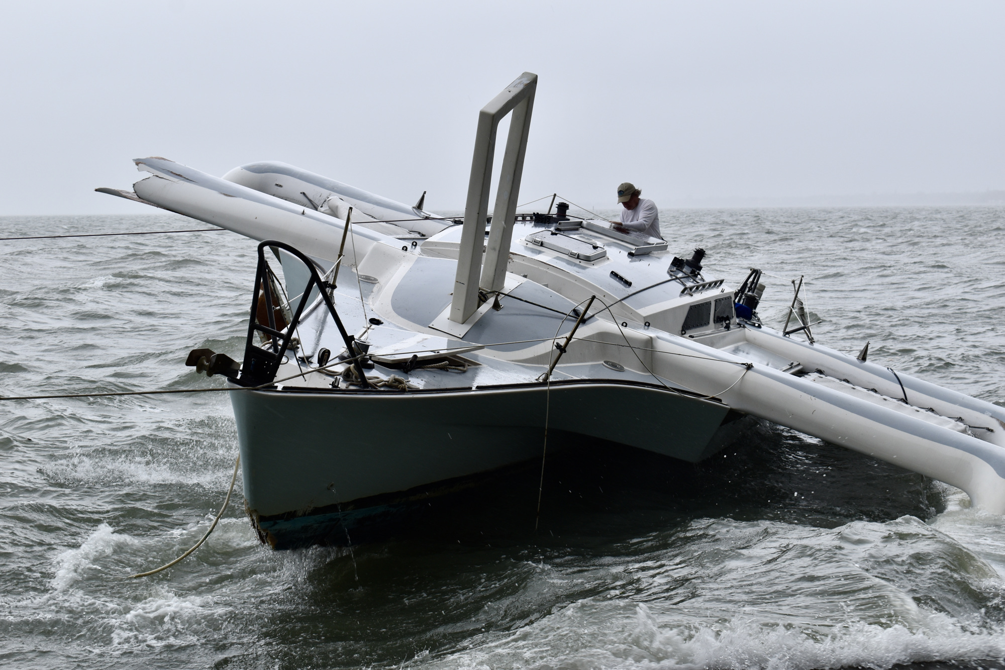 A man aboard a trimaran sailing boat works with a crew on shore to secure the vessel after it was driven against the seawall at Hart's Landing. (Eric Garwood)